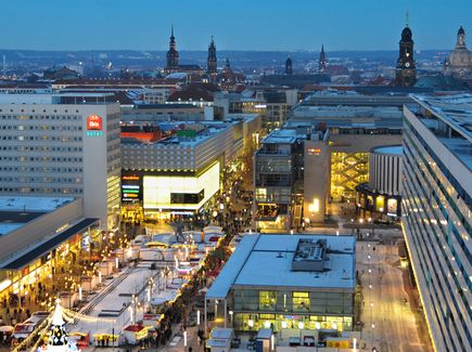 Die Prager Straße in Dresden zu Weihnachten ist abgebildet. Es ist abends und Lichter leuchten. 