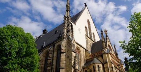 Die Thomaskirche in Leipzig ist von außen zu sehen. Neben der Kirche stehen zwei Bäume.