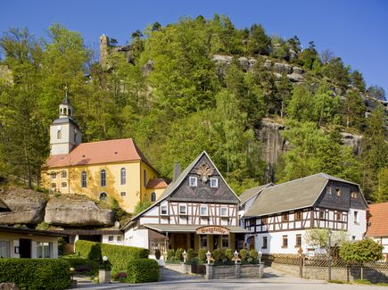 Die Bergkirche in Oybin ist abgebildet. Hinter den Kirche ist ein Hügel mit Bäumen und neben der Kirche Häuser. 