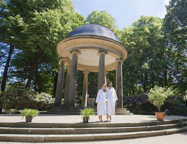 Ein kleiner Tempel steht im Park von Bad Elster. Davor laufen zwei Menschen vorbei.