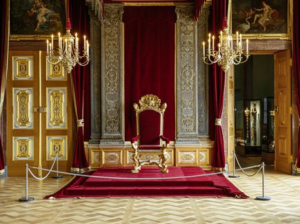 Die Königlichen Paraderäume Augusts des Starken im Residenzschloss Dresden Ein großer, prunkvoller Raum mit einem roten Thron in der Mitte. Von der Decke hängen drei goldene Kronleuchter.