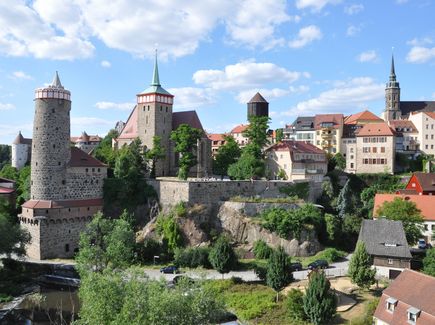 Das Altstadtpanorama von Bautzen ist abgebildet. Zwischen den Gebäuden stehen Bäume.